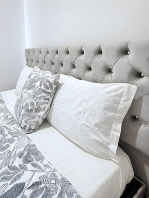 A bed with a tufted headboard, white bedding, and patterned pillows. - Apartment 'House Guest Confort Vila Minde' with Wi-Fi and Air Conditioning (Minde)