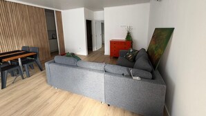 En moderne stue med en grå hjørnesofa, et træspisebord med stole og et rødt skab med en plante.