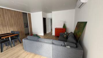 A modern living room with a grey sectional sofa, a wooden dining table with chairs, and a red cabinet with a plant.