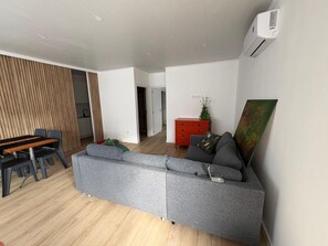 A modern living room with a grey sectional sofa, a wooden dining table with chairs, and a red cabinet with a plant. - Apartment 'House Guest Confort Vila Minde' with Wi-Fi and Air Conditioning (Minde)