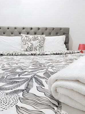 A bed with a tufted headboard, patterned bedding, and a red bedside lamp.