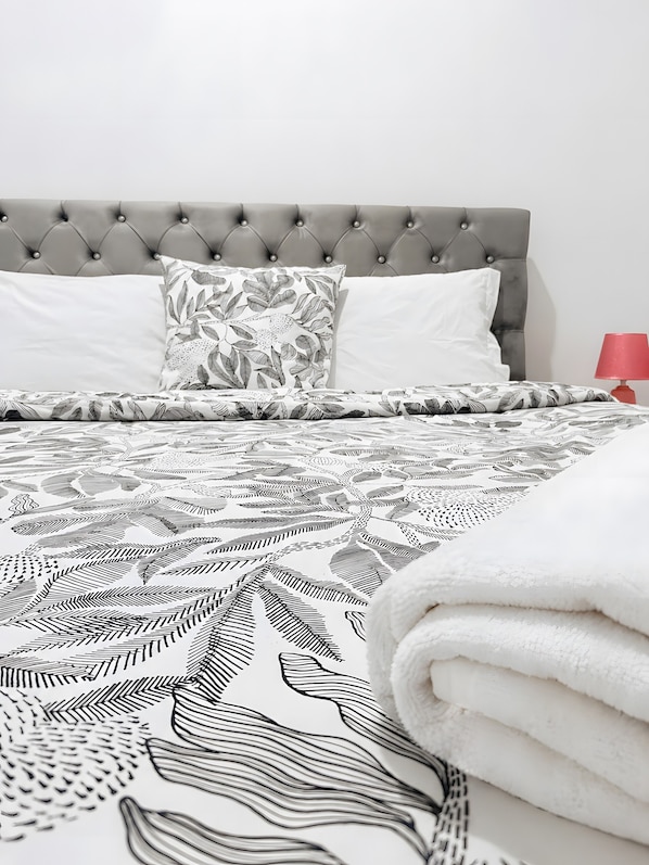 A bed with a tufted headboard, patterned bedding, and a red bedside lamp. - Apartment 'House Guest Confort Vila Minde' with Wi-Fi and Air Conditioning (Minde)