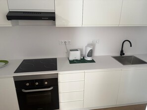 A modern kitchen with white cabinets, a black dishwasher, a built-in oven, a stainless steel sink, and a toaster.