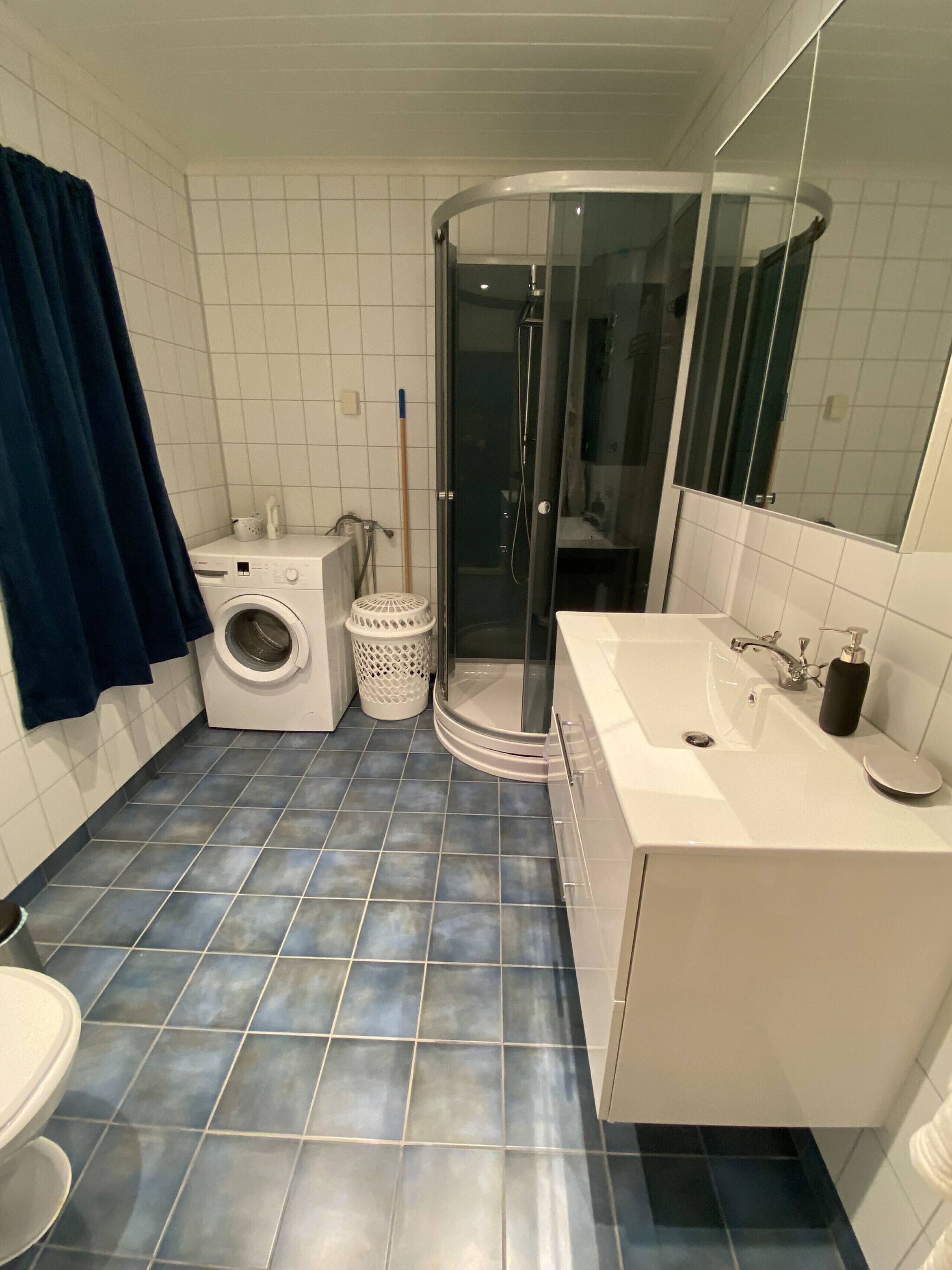 A bathroom with a washing machine, a shower, a sink, and a toilet.