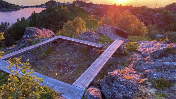 Un paisaje natural con una estructura de madera, posiblemente una terraza o plataforma, rodeada de rocas y vegetación.