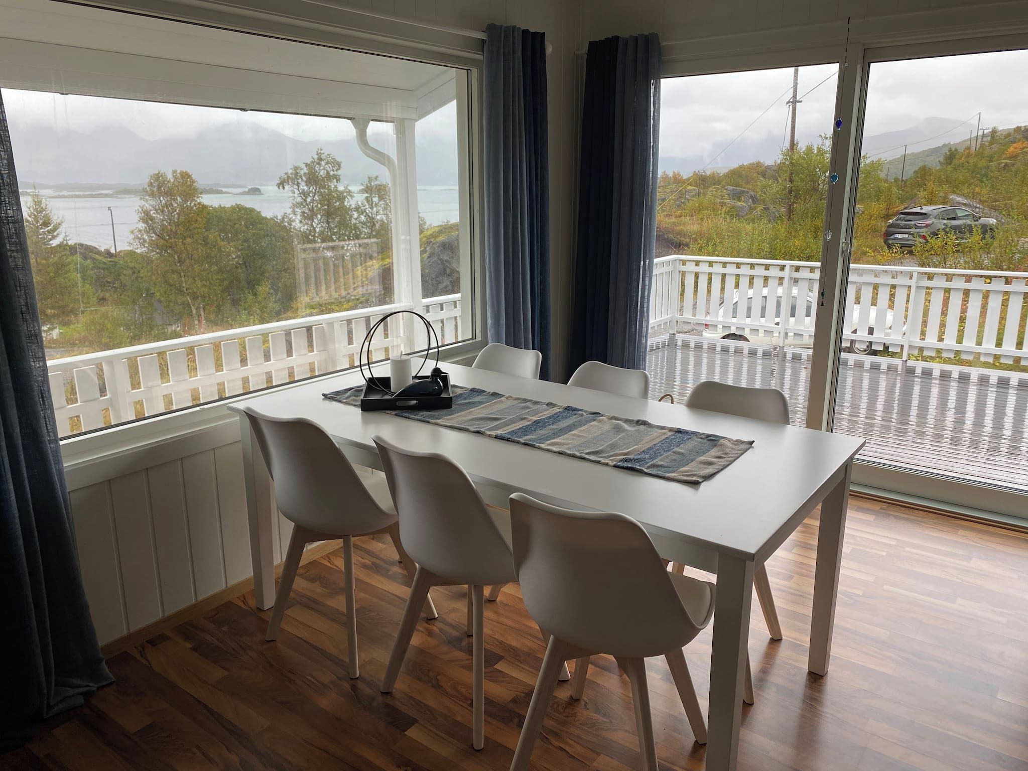 A dining area with a table and chairs, a view of a balcony with a railing, and a glimpse of the outdoors.