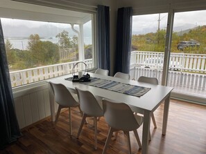A dining area with a table and chairs, a view of a balcony with a railing, and a glimpse of the outdoors.