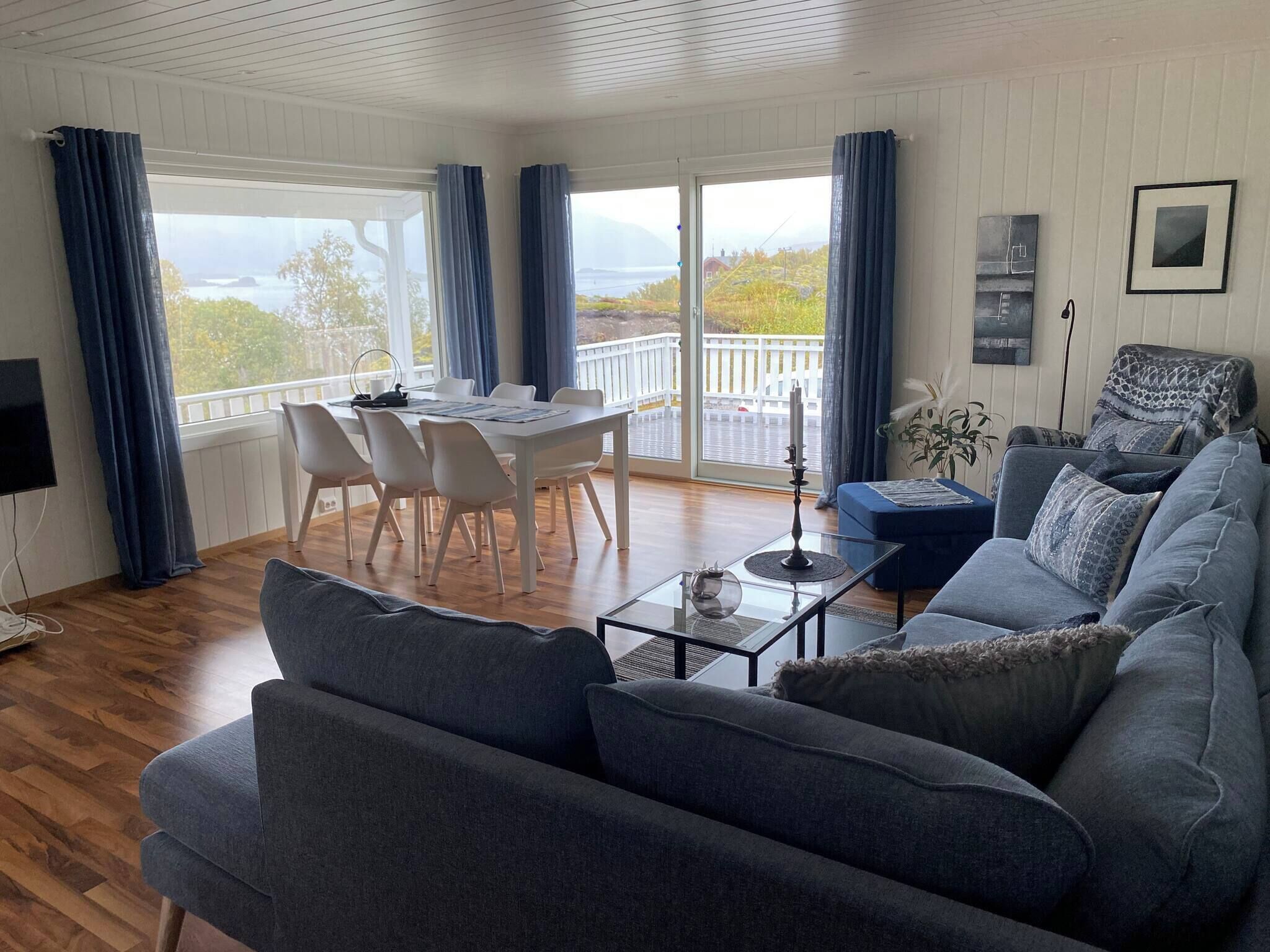 A modern living room with a sofa, a dining table with chairs, and a balcony with a view.