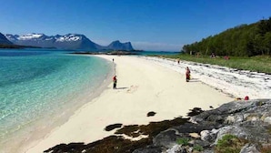 Una playa con agua turquesa cristalina, una orilla arenosa y montañas al fondo.