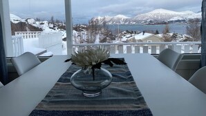 Un comedor con una mesa lista para dos personas, un florero con flores y vistas a montañas nevadas y un lago.