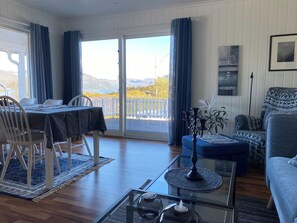 A room with a dining table, chairs, a sofa, a coffee table, and a view of mountains through a large window.