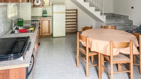 A kitchen with a stove, sink, and cabinets, a dining table with chairs, and a staircase leading to another level.