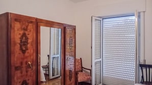 Une pièce comprenant une armoire en bois, une armoire avec des portes miroir, une chaise et une porte-fenêtre coulissante avec des stores.