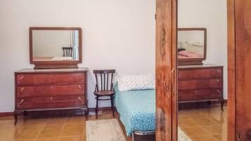 Una camera da letto con due comò in legno, una sedia, un letto con copripiumino blu e uno specchio appeso al muro.
