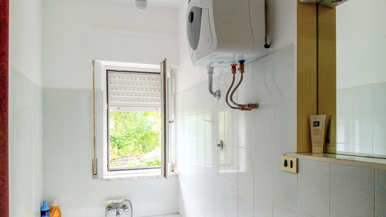 Un bagno con finestra, scaldabagno e dispenser per asciugamani.