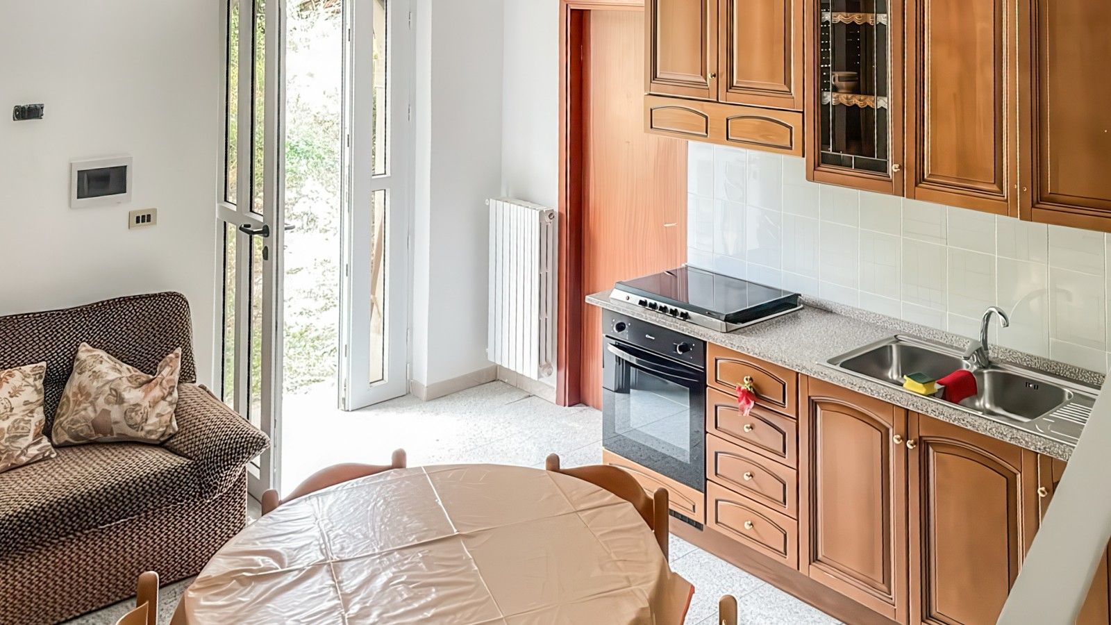 Cozinha compacta com área de refeições, forno embutido e janela com vista para um jardim.