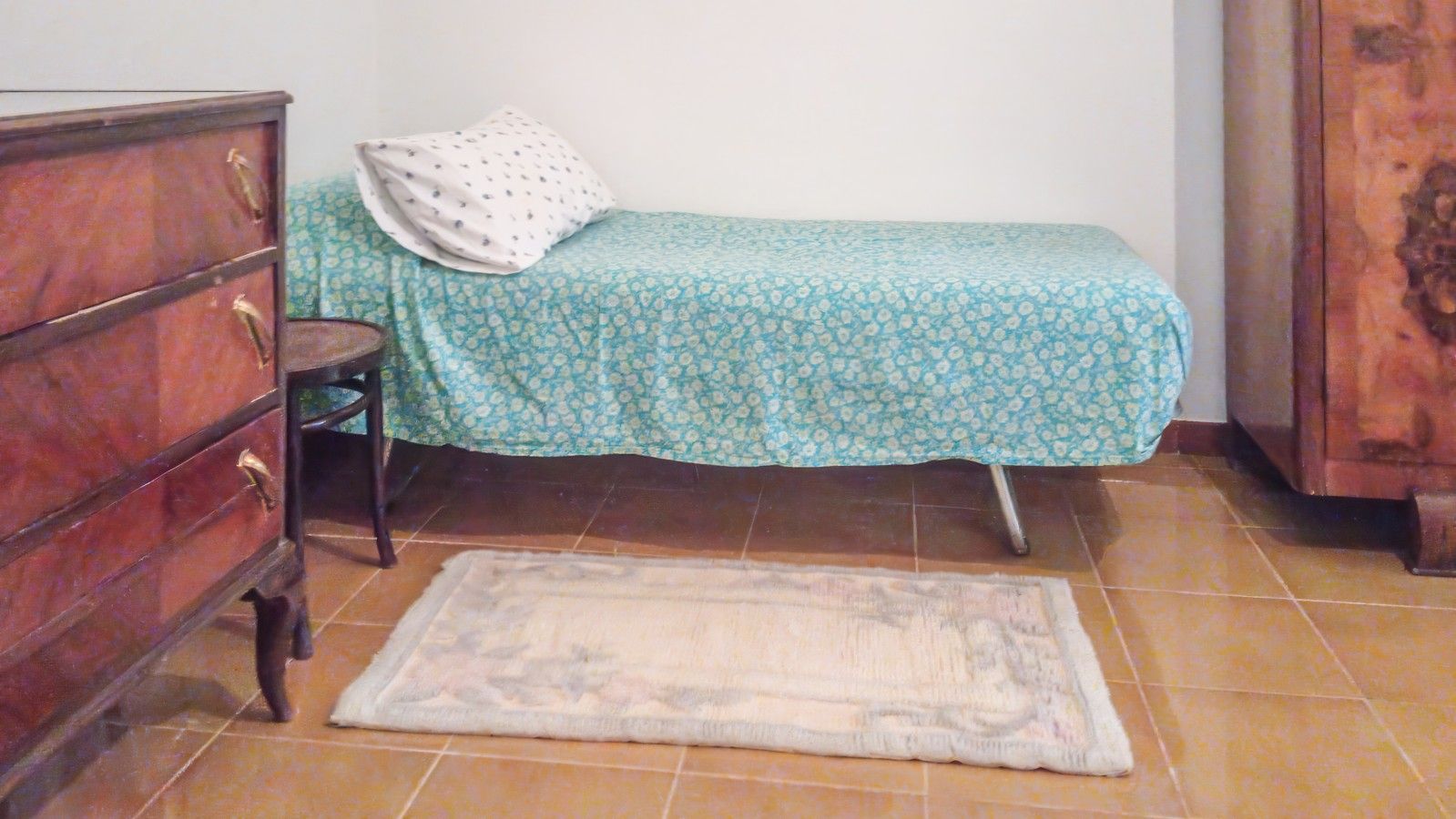 Ein kleines Zimmer mit einem Bett, einer Kommode und einem Teppichboden.