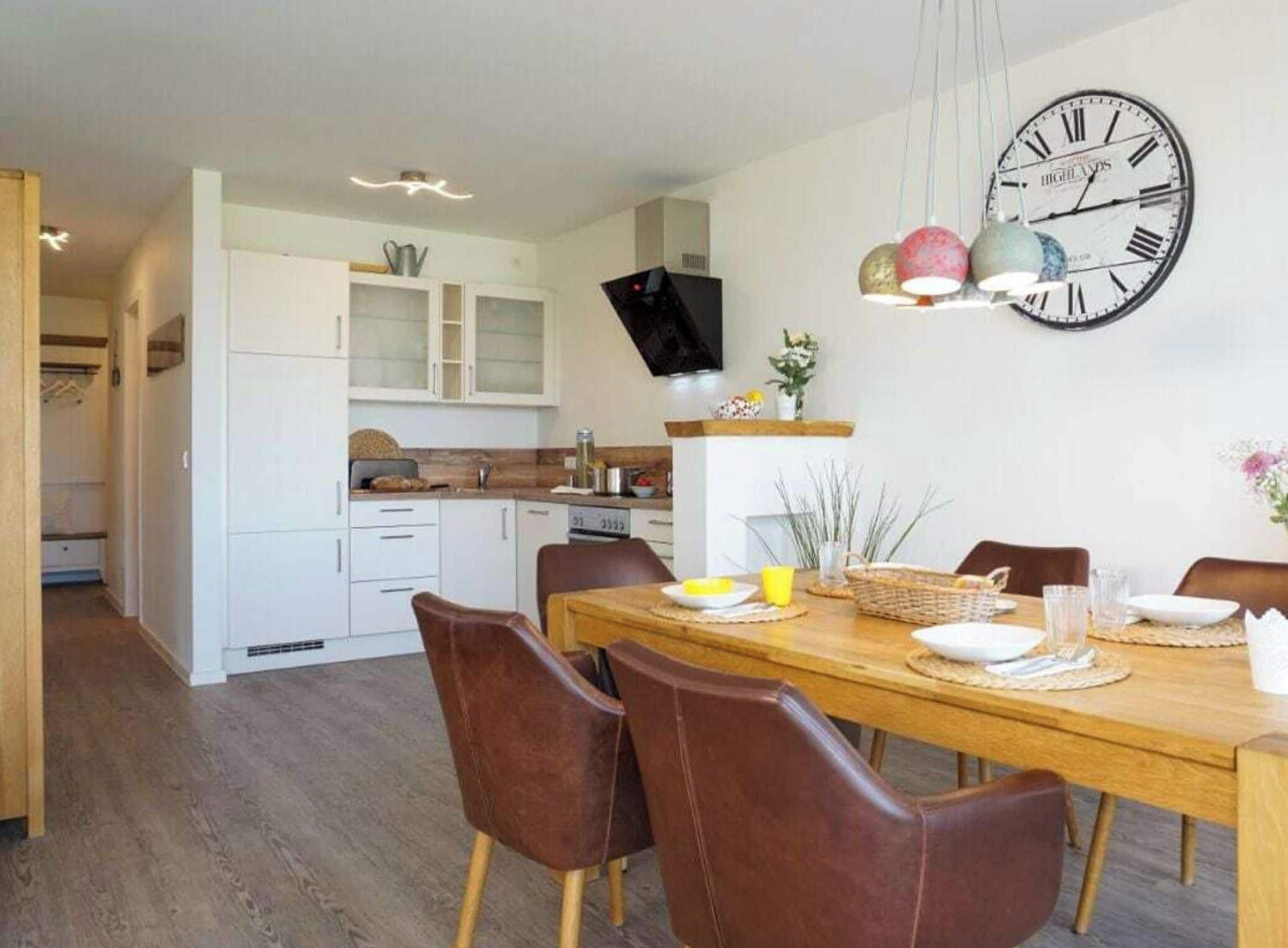 A modern kitchen with white cabinets, a dining table set for four, and a large wall clock.