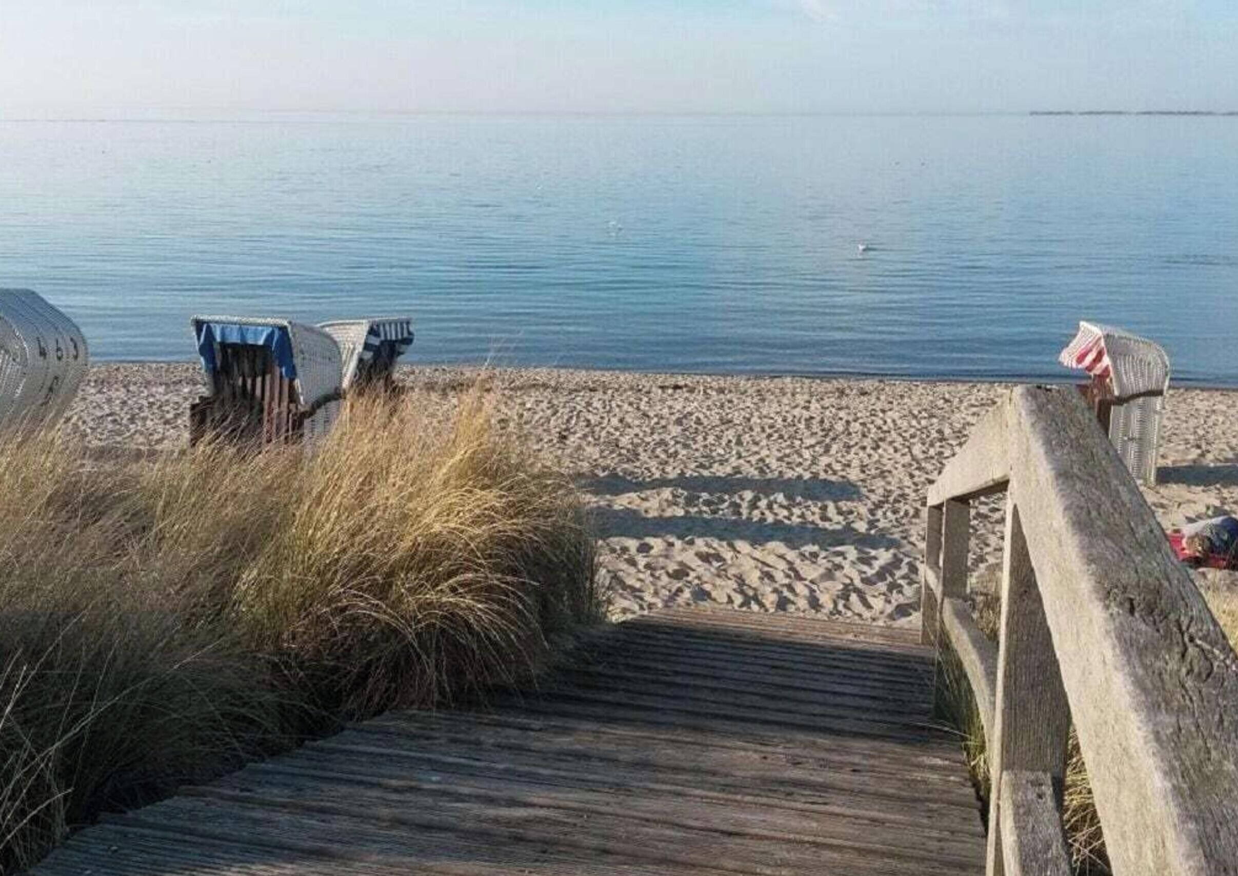 Een houten looppad dat naar een zandstrand leidt, met strandstoelen en een klein gebouwtje.