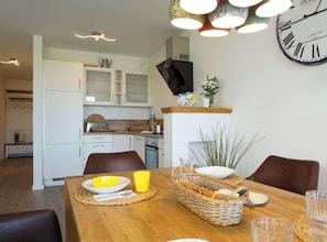 A dining area with a wooden table set for two, a television mounted on the wall, and a clock. - Holiday Apartment With 2 Bedrooms (Heiligenhafen)