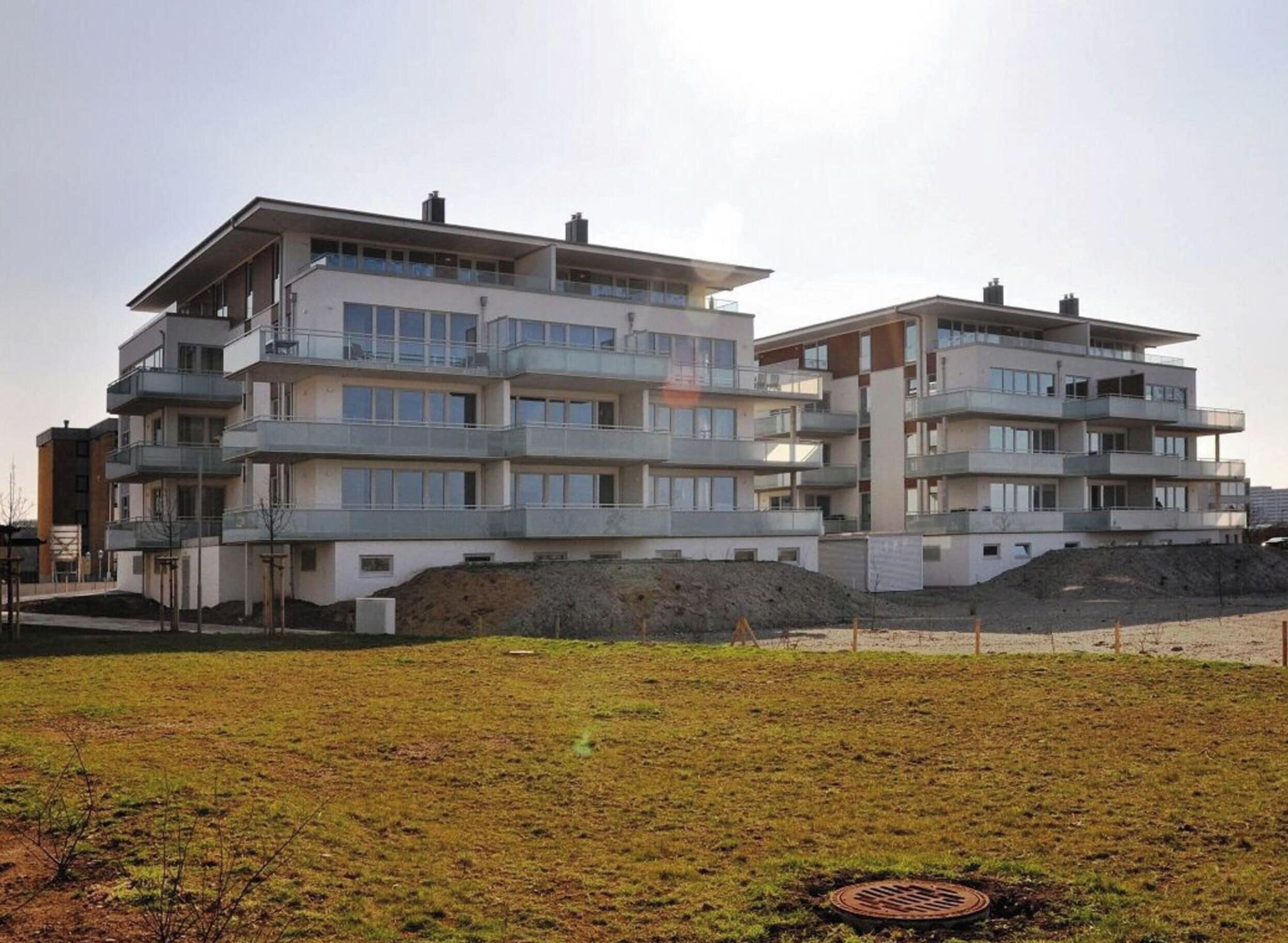Un edificio residencial de varios pisos con balcones, techo plano y un área con césped en primer plano.