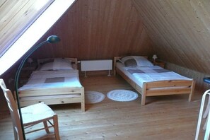 Ein kleines Schlafzimmer im Dachgeschoss mit zwei hölzernen Betten, einem Stuhl und einer Lampe.