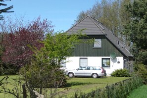 Et hus med en bil foran, omgivet af grønt og træer.