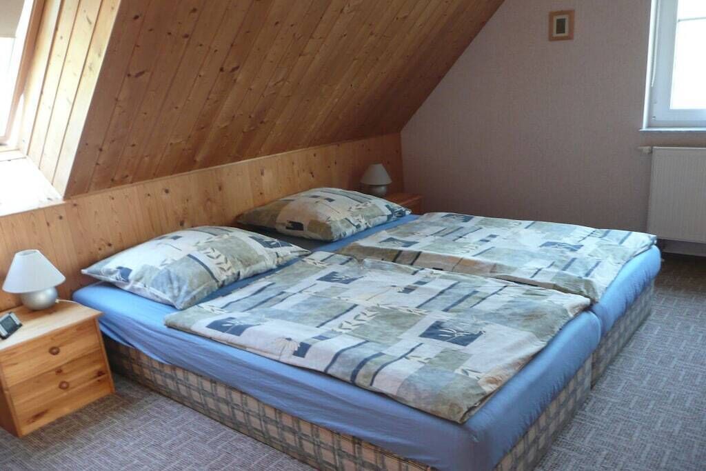 Ein Schlafzimmer mit Schräge, einem Bett mit gemustertem Überwurf, einem Nachttisch mit Lampe und einem Fenster.