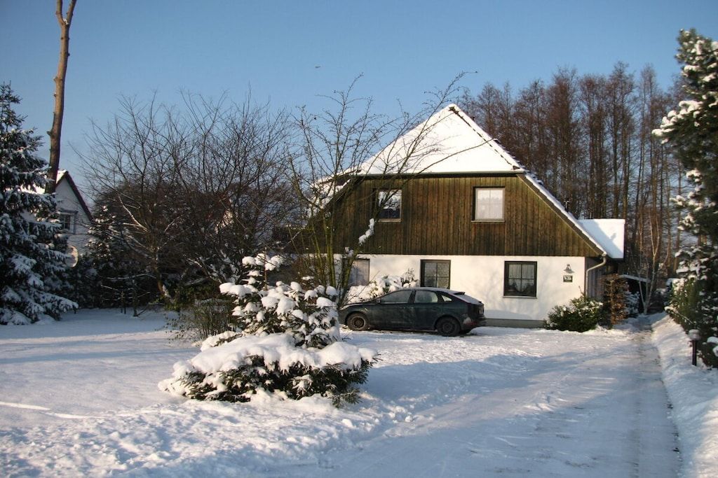 A house with a sloped roof, a car parked in the driveway, and snow on the ground.