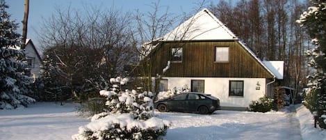 A house with a sloped roof, a car parked in the driveway, and snow on the ground.