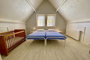 A bedroom with a sloped ceiling, two windows, a crib, and a bed with a checkered bedspread. - Holiday home in Wapse with swimming pool (Wapse)