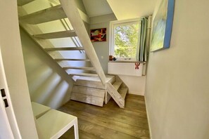 Eine Holztreppe führt zu einem Schlafzimmer auf dem Dachboden, mit einem Fenster mit Blick auf Grünflächen.