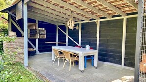 A covered outdoor patio with a table and chairs, a hanging light fixture, and a brick wall. - Holiday home in Wapse with swimming pool (Wapse)
