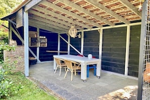 A covered outdoor patio with a table and chairs, a hanging light fixture, and a brick wall. - Holiday home in Wapse with swimming pool (Wapse)