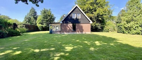 Une maison aux murs en briques et au toit à pignon, entourée d’une pelouse bien entretenue et d’arbres.