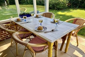 An outdoor dining area with wicker chairs and a wooden table set for a meal. - Holiday home in Wapse with swimming pool (Wapse)