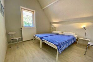 Ein Schlafzimmer mit einem Bett, einem Sessel, einem Nachttisch, einer Lampe und einem Fenster.