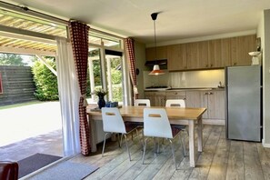 A modern kitchen with a dining area, wooden cabinets, a stainless steel refrigerator, and a large window with curtains. - Holiday home in Wapse with swimming pool (Wapse)