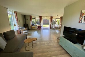 A living room with a sofa, two small tables, a TV on a cabinet, and a dining area with chairs and a table. - Holiday home in Wapse with swimming pool (Wapse)