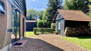 A gravel pathway leading to a wooden cabin with a tiled roof, surrounded by a well-maintained lawn and a hedge. - Holiday home in Wapse with swimming pool (Wapse)