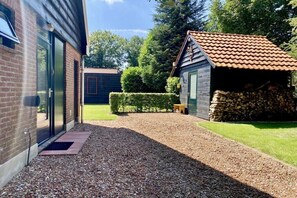 A gravel pathway leading to a wooden cabin with a tiled roof, surrounded by a well-maintained lawn and a hedge. - Holiday home in Wapse with swimming pool (Wapse)