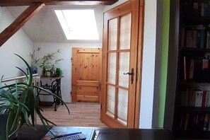 A room with a sloped ceiling, a wooden door, a bookshelf, and a table with a calculator and books.