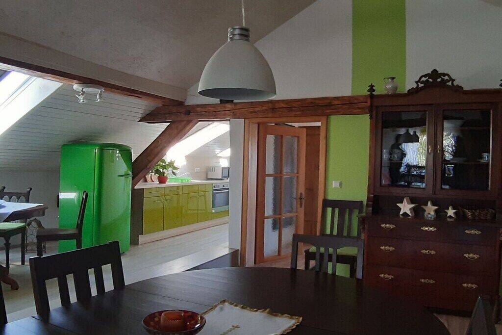 Un coin repas comprenant une table, des chaises, un réfrigérateur vert, un meuble en bois et un luminaire fixé au plafond.