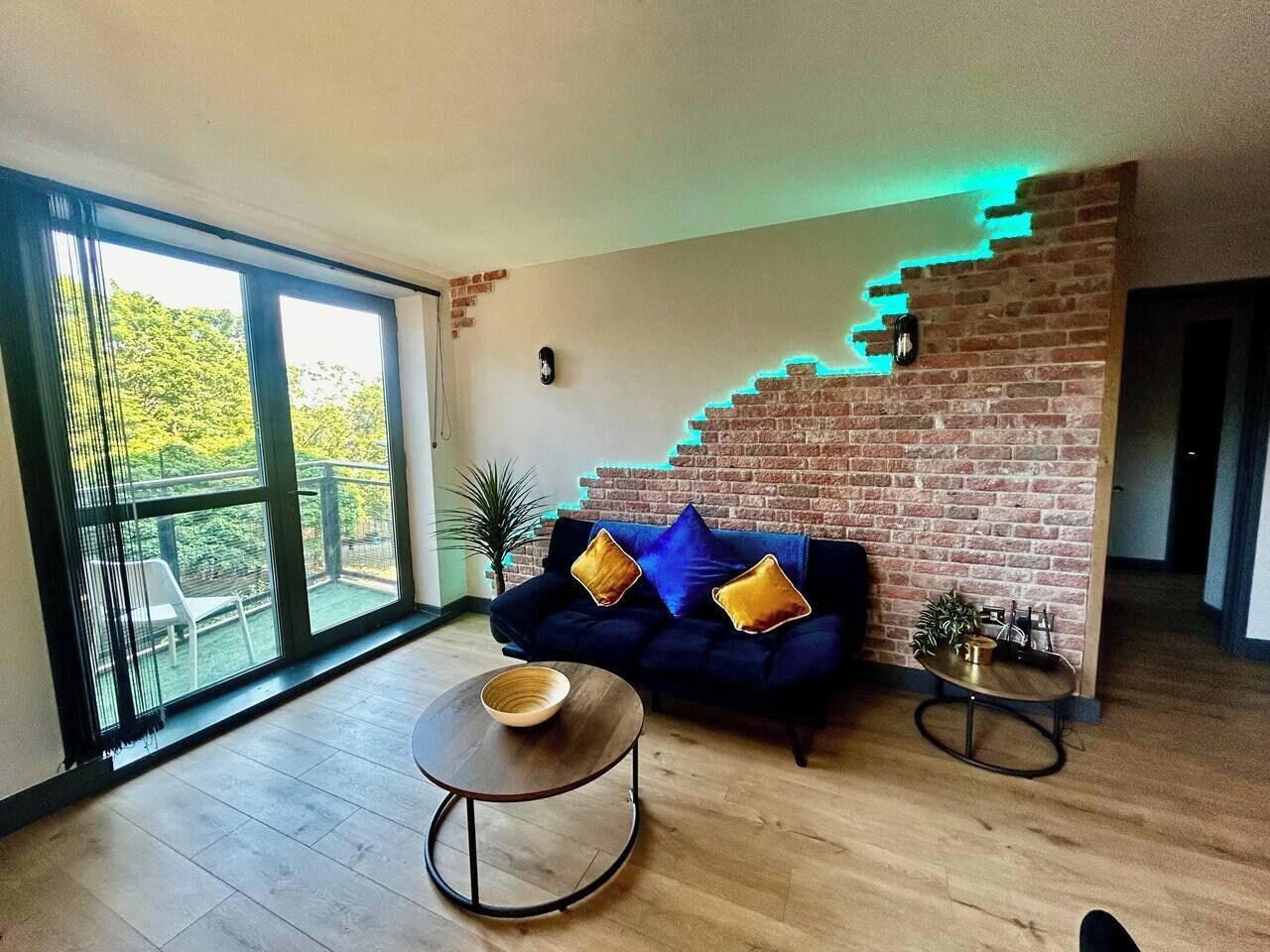 Ein modernes Wohnzimmer mit einer Ziegelfassade, einem dunkelblauen Sofa mit Kissen, einem runden Couchtisch und einem kleinen Beistelltisch mit einer Pflanze.