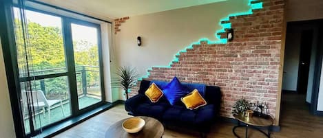 A modern living room with a brick accent wall, a dark blue sofa with cushions, a round coffee table, and a small side table with a plant.