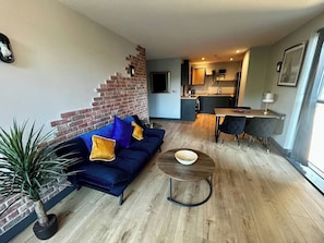 A living room with a blue sofa, a round coffee table, and a brick accent wall.