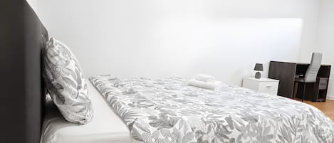 A modern bedroom with a bed, a nightstand, a desk, and a chair.