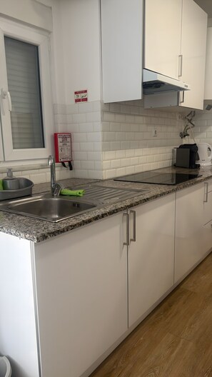 A kitchen with white cabinets, a stainless steel sink, a built-in stove, and a window with blinds.