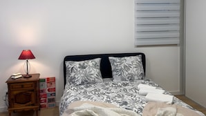 Une chambre à coucher avec un lit, une table de chevet avec une lampe, une fenêtre avec des stores et un climatiseur fixé au mur.