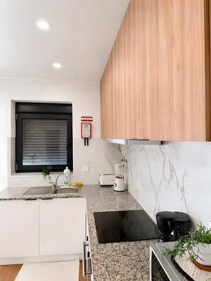 A modern kitchen with white cabinets, a black induction cooktop, a built-in oven, and a window with blinds. - Apartment 'Mira D'Aire Serenity House Confort' (Mira de Aire)